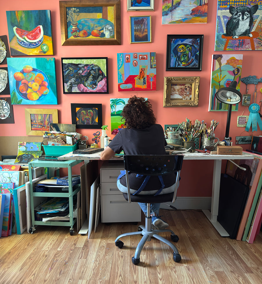Terry Pesso sitting at a desk in a colorful art studio with various paintings on the wall. Color-driven original artwork and contemporary painting by Terry Pesso created in acrylic and mixed media. Ready for framed art and framed wall art as vibrant wall art decor for modern interiors.