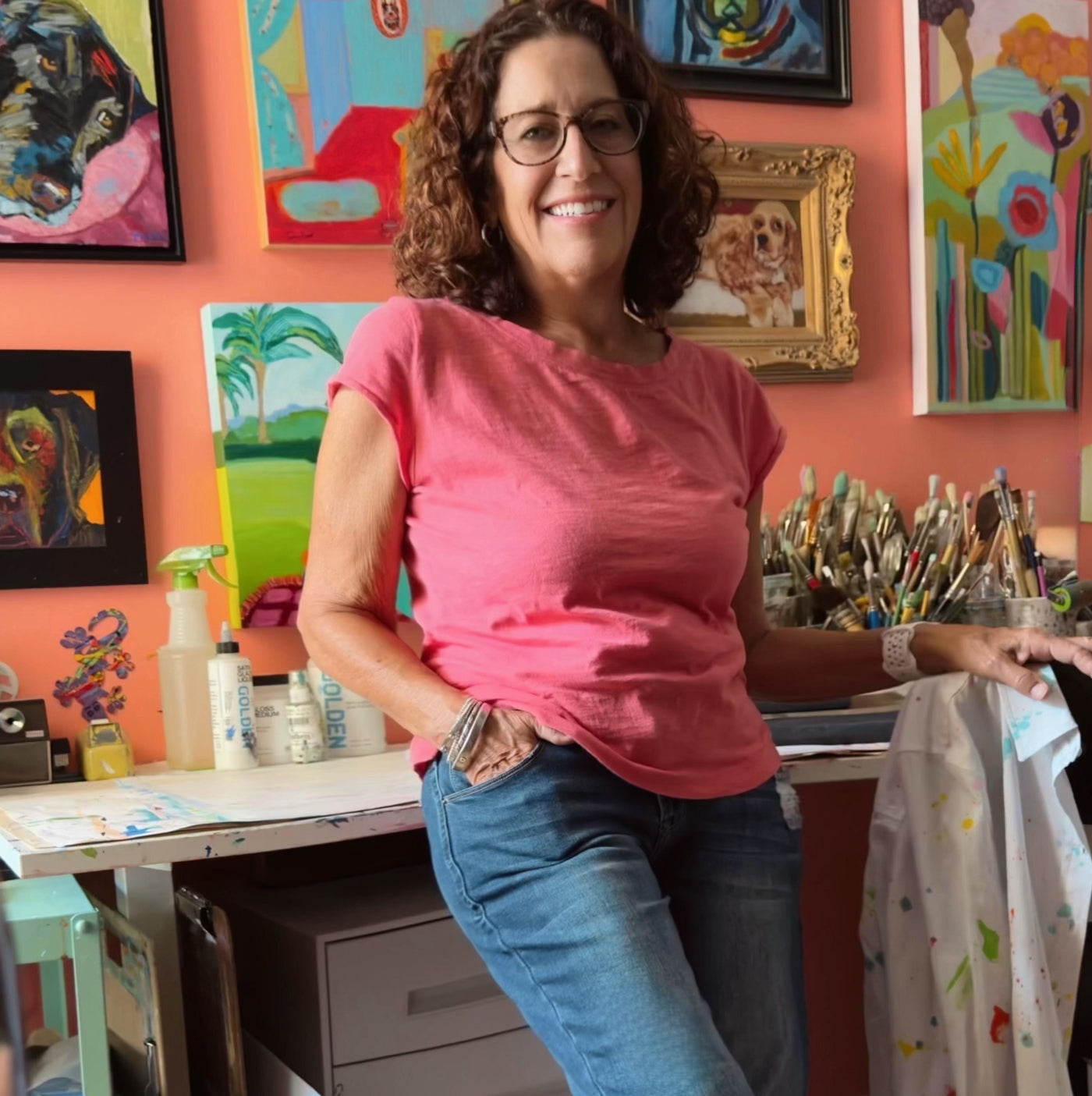Woman in a pink shirt standing in an art studio with colorful paintings on the wall. Original painting by Terry Pesso created as collectible artwork for wall art decor. This contemporary mixed media piece is suitable for framed art and framed wall art in modern homes.