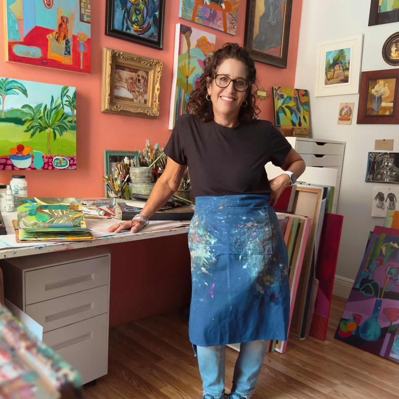 Woman in an art studio with colorful paintings on the walls and a desk. Original artwork and contemporary painting by Terry Pesso featuring bold color and expressive mixed media style. Suitable for framed art and framed wall art as modern wall art decor for collectors.