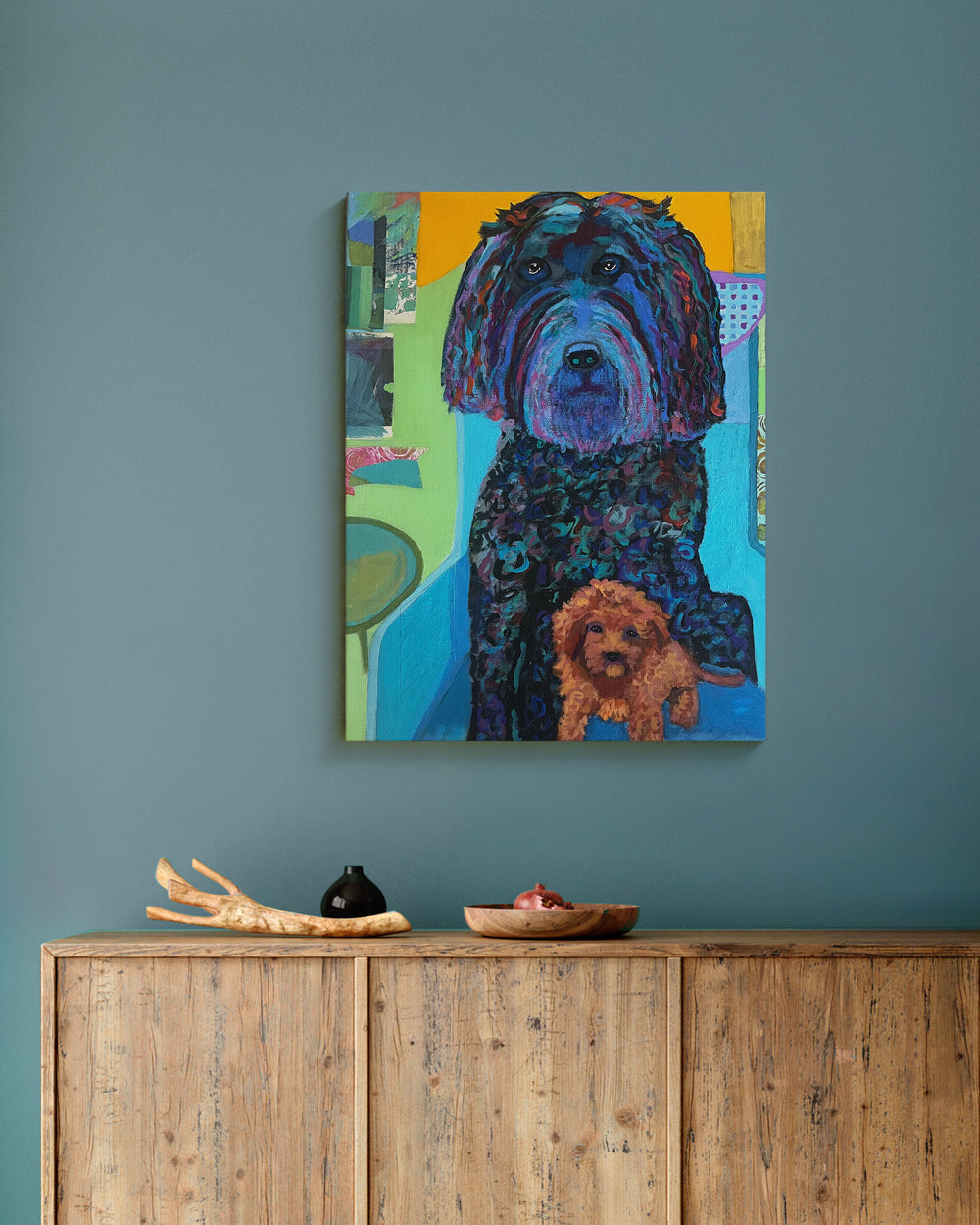 Colorful painting of a dog on a wall above a wooden cabinet. Lifestyle mockup view. "I'm Not Sharing" is an original mixed media painting featuring two dogs Ñ a large Labradoodle and a playful Toy Poodle — captured in expressive color and texture. Bold strokes of turquoise, indigo, and orange create a lively, layered portrait full of personality. The piece blends humor and affection, celebrating the charm, curiosity, and loyal companionship of dogs in everyday life. A joyful original artwork for dog lovers 