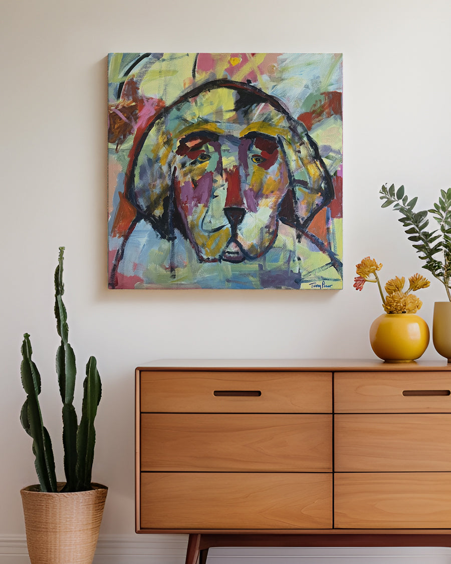 Colorful abstract painting of a dog's head on a wall above a wooden dresser with decorative items. Lifestyle mockup view. "I'm With You" is an original acrylic painting that captures the soulful presence of a dog through bold color and expressive brushwork. Layers of gold, violet, and coral blend together in a composition that feels both modern and deeply emotional. This original artwork celebrates the quiet bond, warmth, and companionship that dogs bring into our lives.